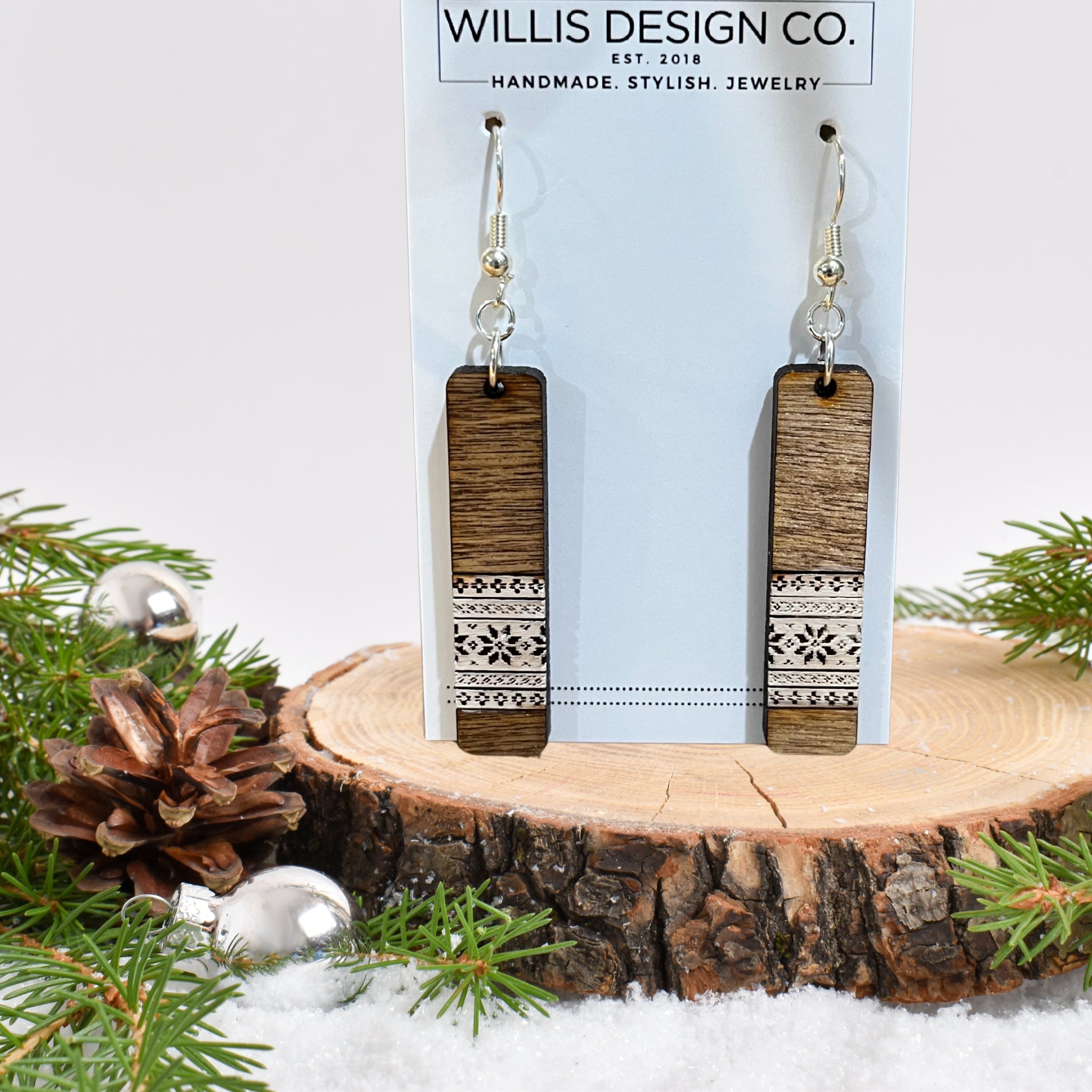 A pair of rectangular drop earrings with a dark wood grain top half and a white geometric patterned bottom half, hanging from silver hooks on a light blue display card. The card is labeled 'WILLIS DESIGN CO.